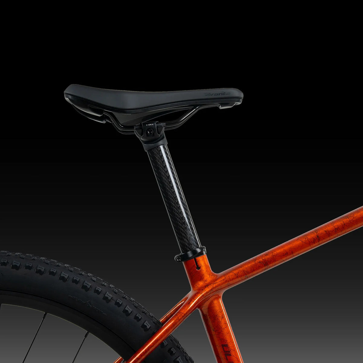 A close up of an orange glossy mountain bike saddle and seatpost on a dark background