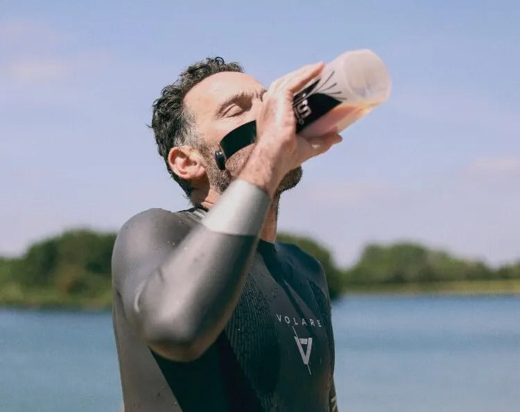 Man drinking hydration from a bottle by a lake .