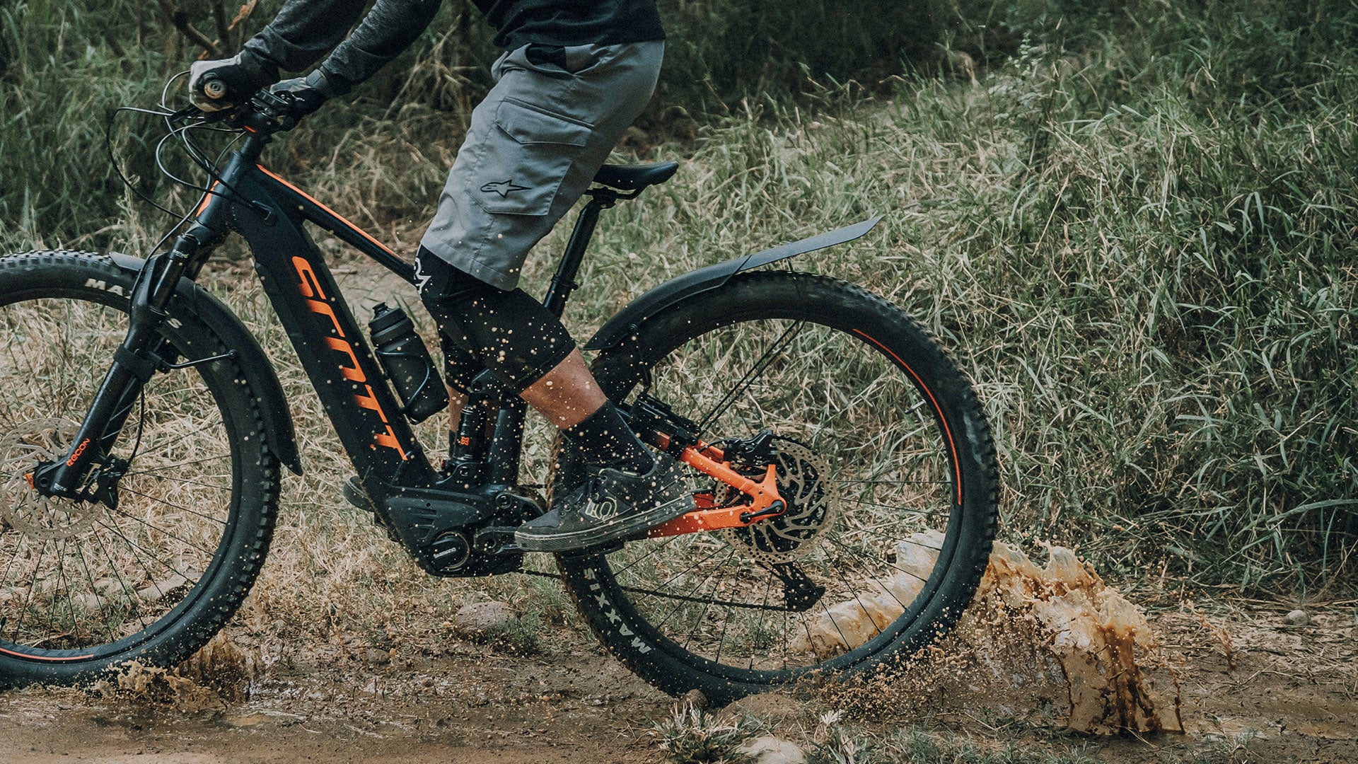 A picture of the  Topeak Tetrafender M1 / M2 Set MTB Fork/Stay Mount Mudguards mounted on a mountain bike and someone riding the bike through mud.